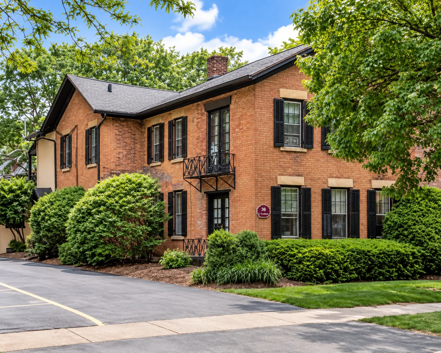 Red-brick multi-family home with black shutters and a wrought-iron balcony at 36 S. Goodman St. in Rochester, NY